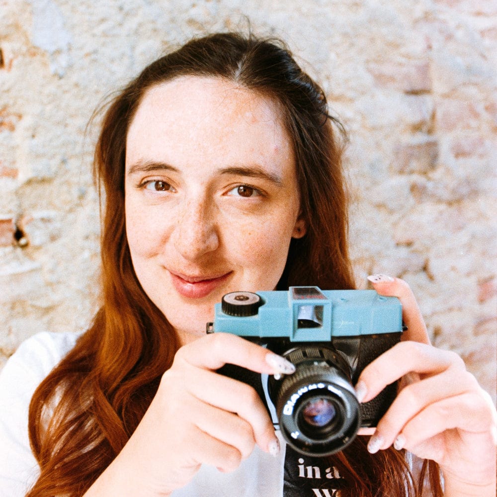 Woman holding a vintage camera against a textured wall.